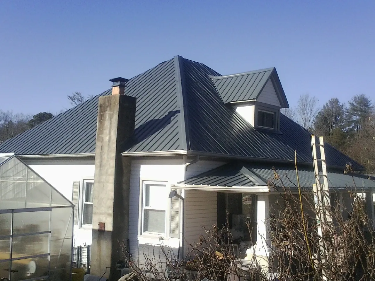 Dark blue standing seam metal roof on a white farmhouse with dormer — Slate & Tile Roof Repair by Roofing Brothers in Prairie Village