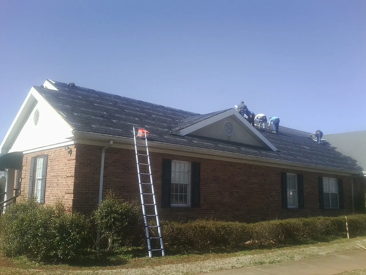 Crew tearing shingles off a brick ranch roof with a ladder set — Emergency Roof Repair work by our crew in Prairie Village