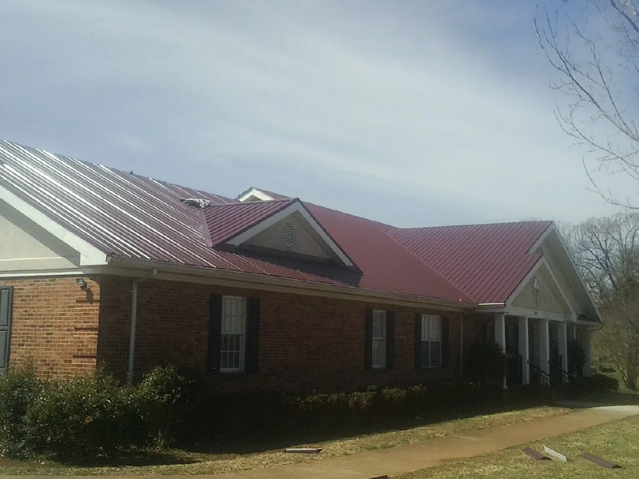 Red metal roof with gabled entries on a long brick building, from a Hail Damage Roof Repair job in Prairie Village