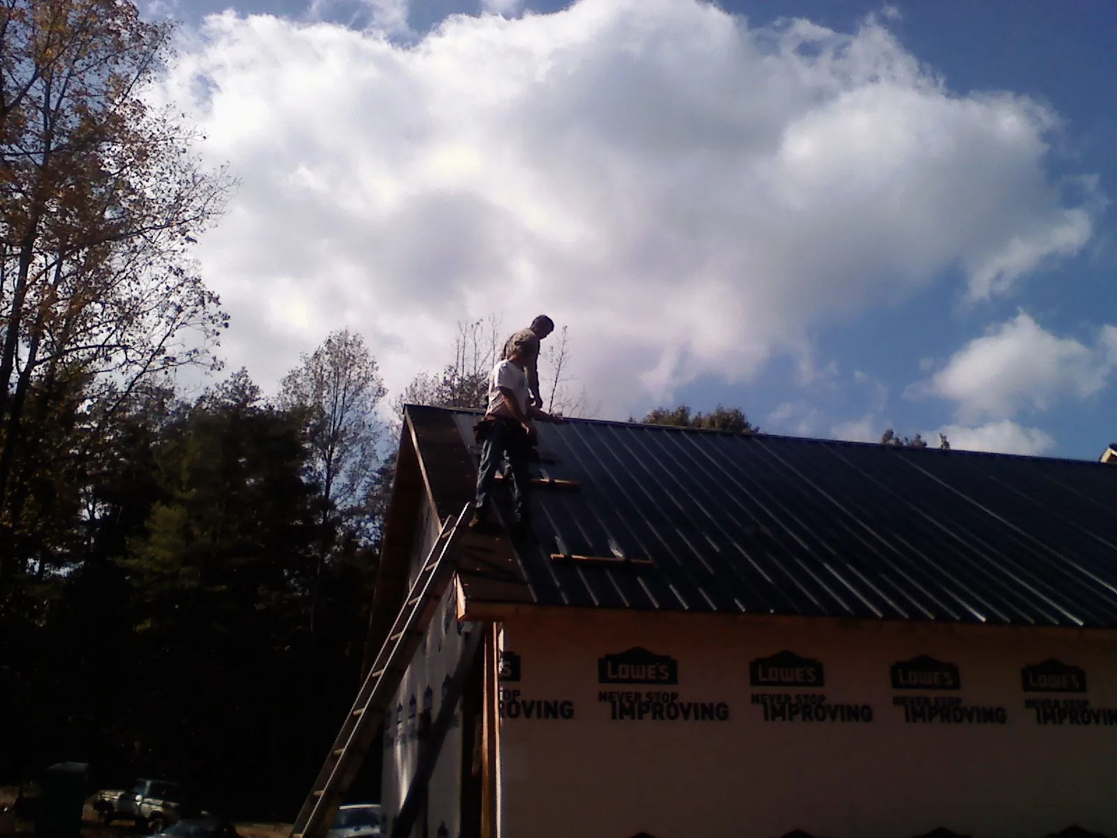 Roofer fastening dark metal panels high against a cloudy sky, from a Roof Inspection job in Prairie Village
