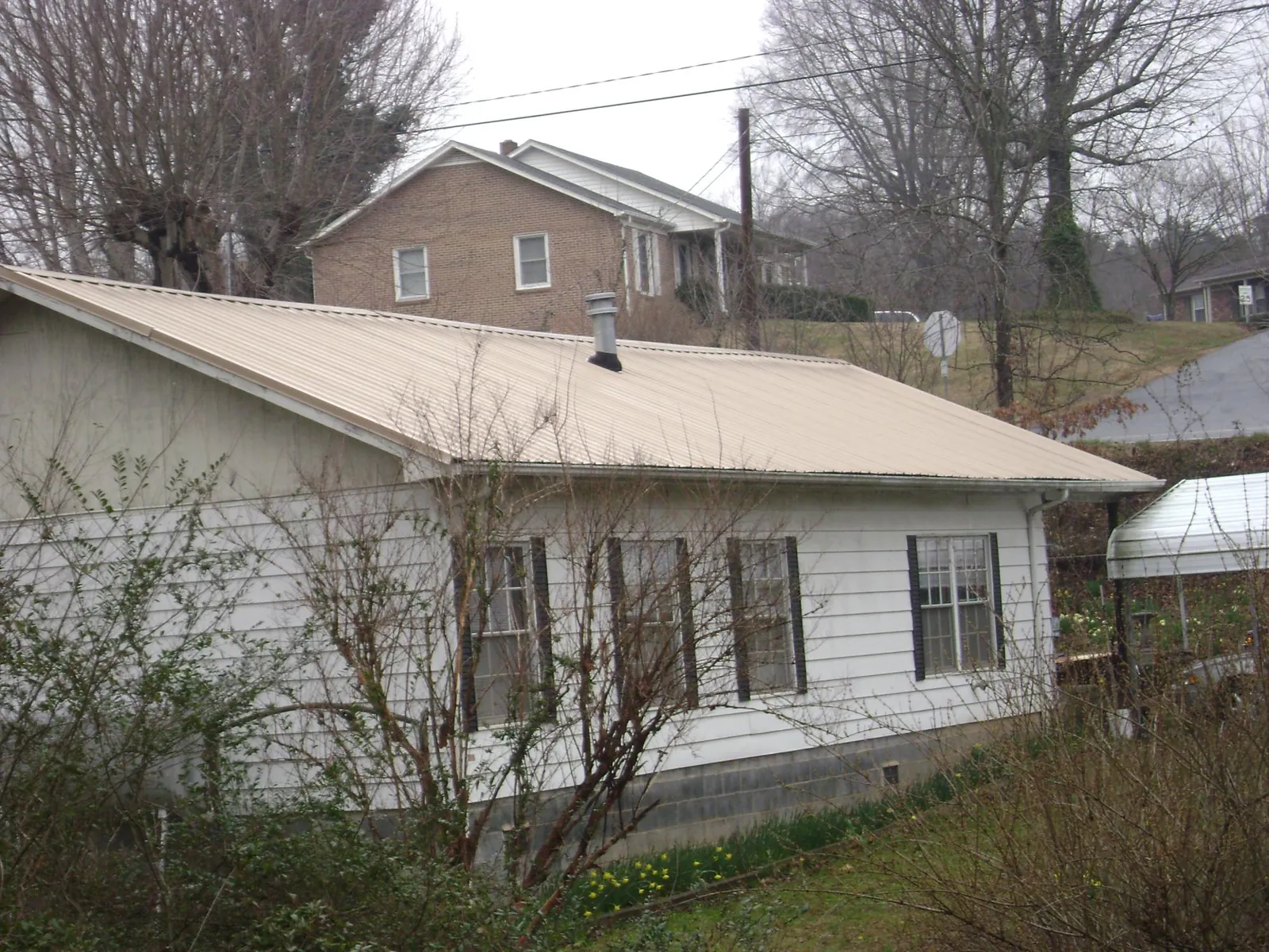 Tan metal roof on a white sided house set into a hillside — Commercial Roofing by Roofing Brothers in Prairie Village