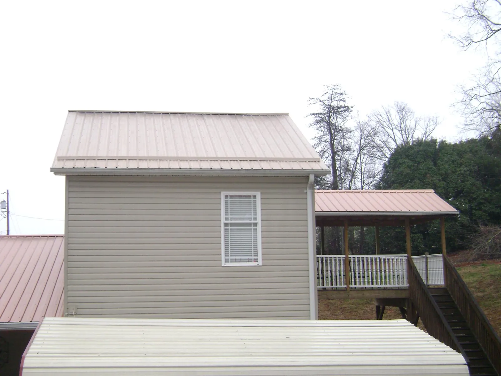 Tan metal roofs on a two story addition and attached porch, from a Roof Replacement job in Prairie Village